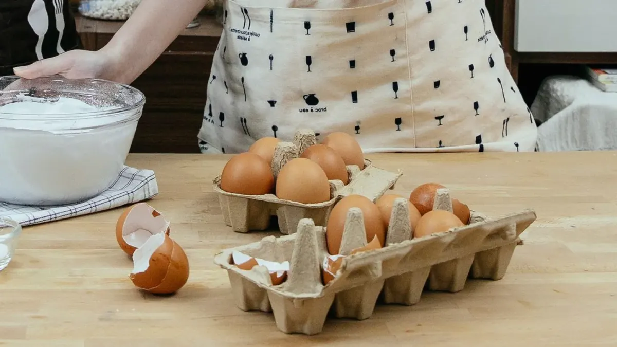 A bowl of plain scrambled egg beside two whole raw eggs on a kitchen counter
