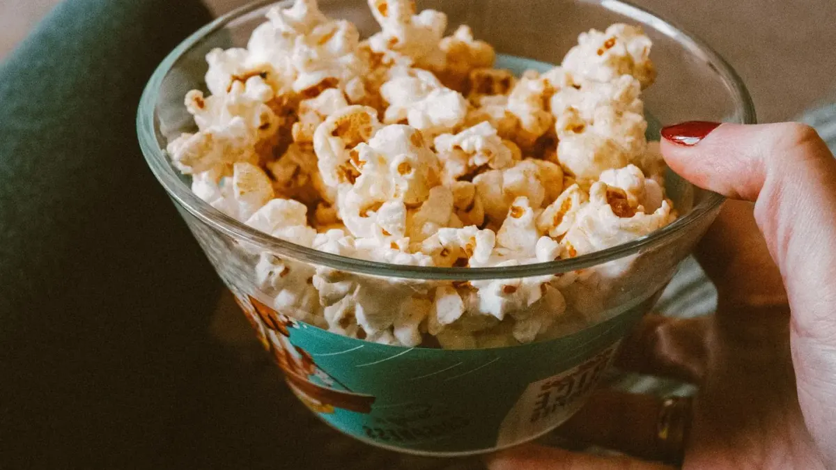 A dog sitting on a couch next to a bowl of plain popcorn