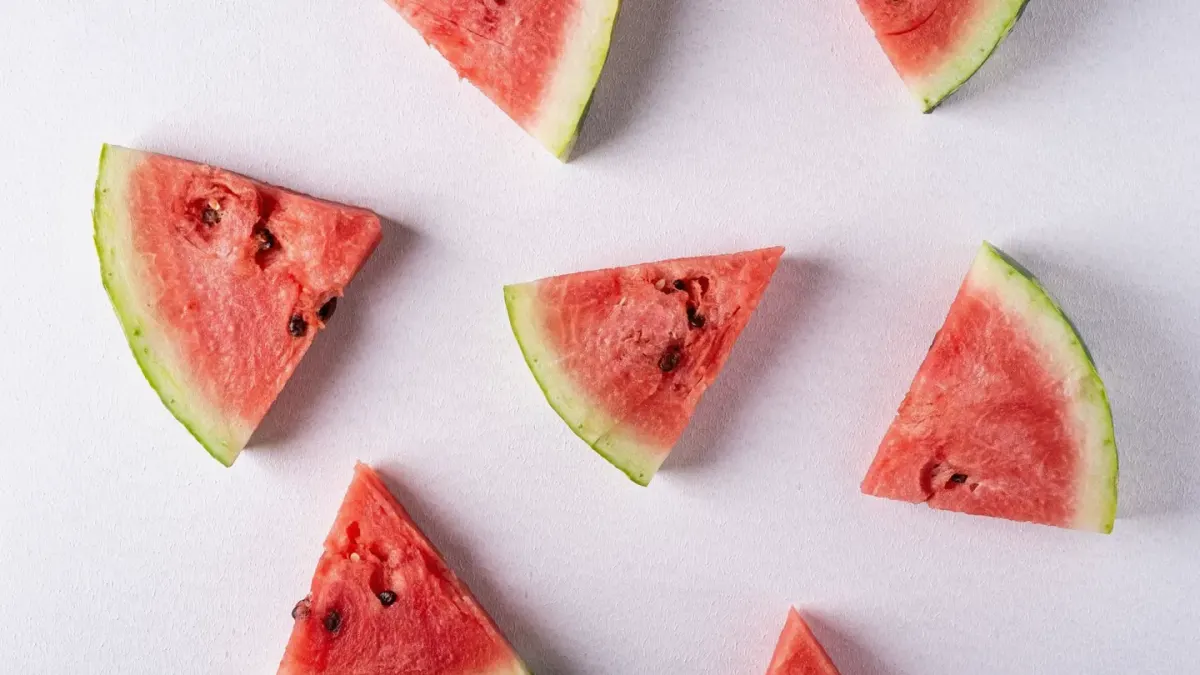 A dog standing beside a cutting board of sliced watermelon on an outdoor table