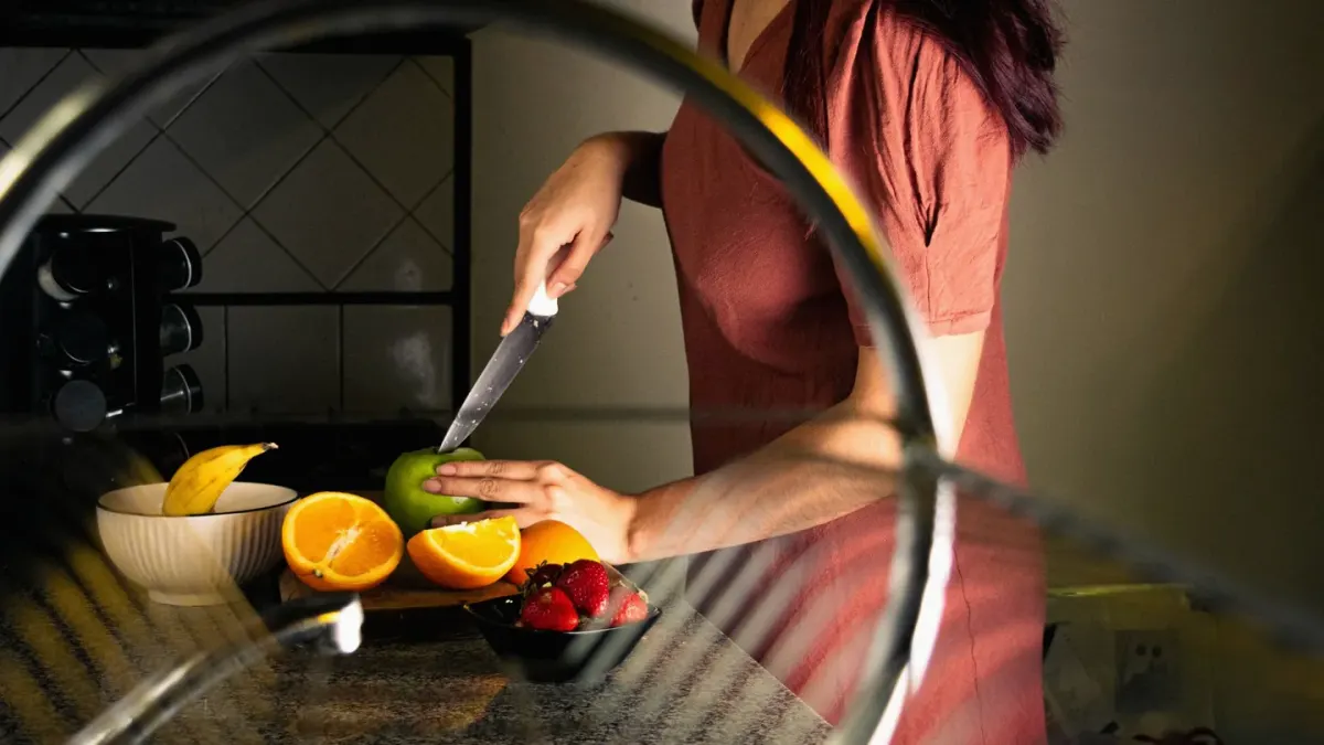 A person slicing an apple into small pieces on a cutting board while a dog waits nearby