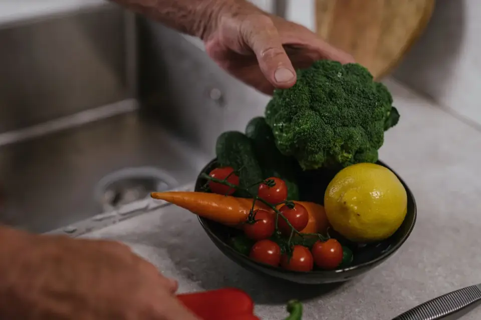 A senior dog eating a small bowl of plain cooked vegetables at home