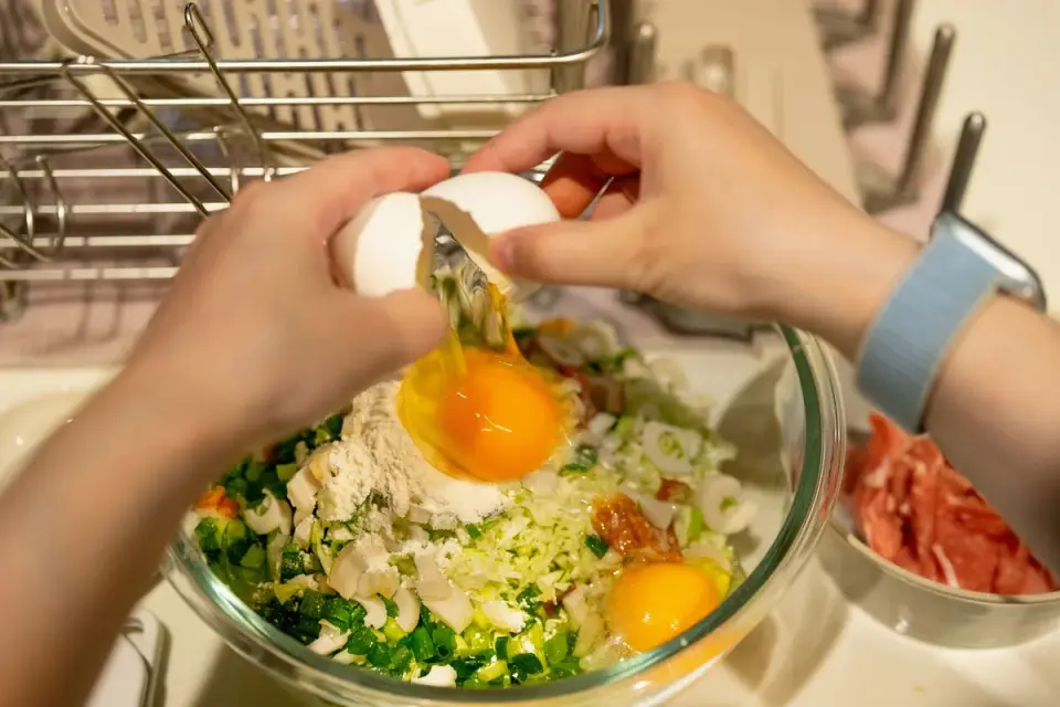 Golden retriever watching an owner crack eggs into a mixing bowl on a kitchen counter