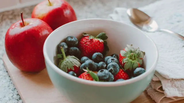 Sliced apples, carrots, blueberries, and green beans arranged near a dog's food bowl