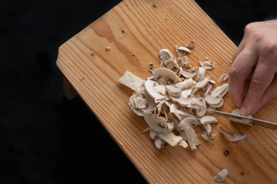 Sliced cremini mushrooms on a cutting board beside a dog&#x27;s food bowl