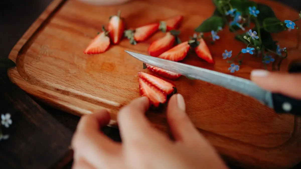 Sliced fresh strawberries arranged next to a dog's stainless steel bowl on a kitchen counter